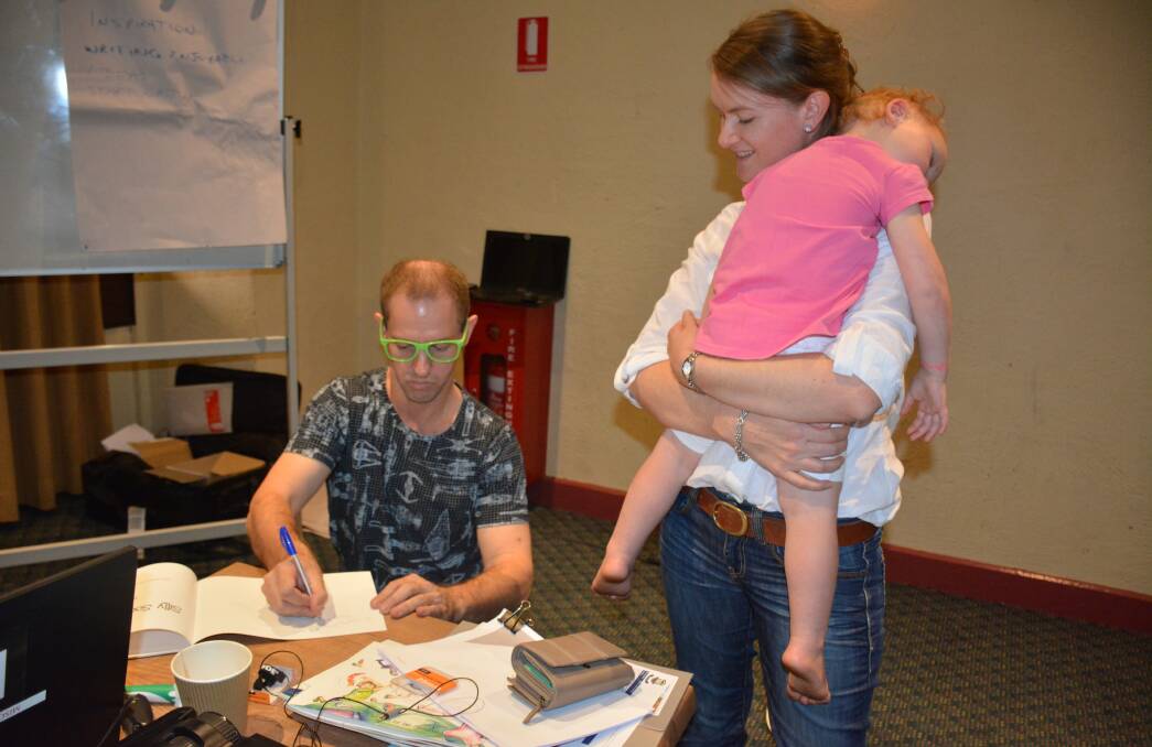 Children's book author Ian McIntosh signs a copy of a book for Catherine Woodhouse and her tired daughter Claire, 2. Photo: Chris Burns. 