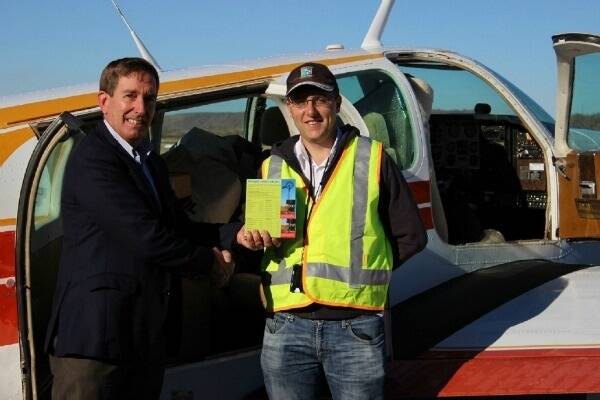 Chair of NWHH Board Chair Paul Woodhouse handing over the Drought Crisis Contacts postcard for delivery in the North and West by Savannah Air pilot, Daniel Ball, on the West Wing mail run.