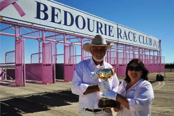 Bedourie Race Club President and Secretary, Garth and Kathi Tully, stand with the newly-painted pink barriers, which are part of the ‘dress the desert pink’ breast cancer initiative. 